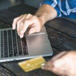man-s-hand-holding-credit-card-typing-laptop-wooden-desk.jpg